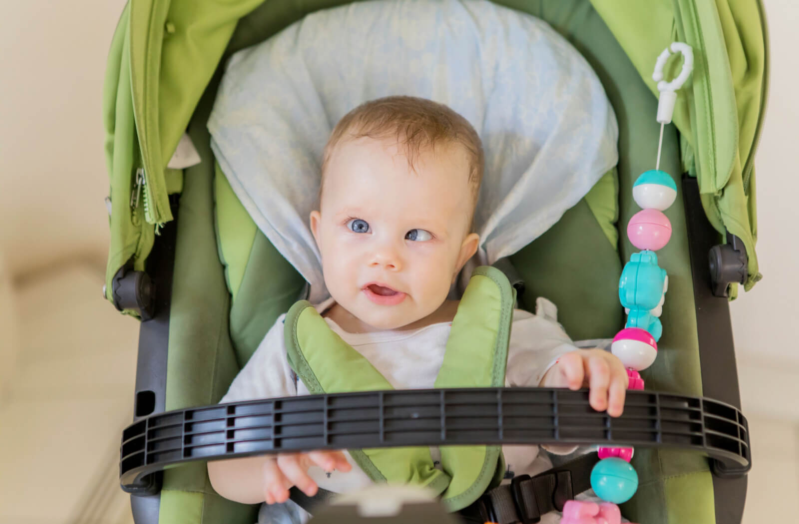 A baby boy is sitting in his green carrier with his eyes crossed.