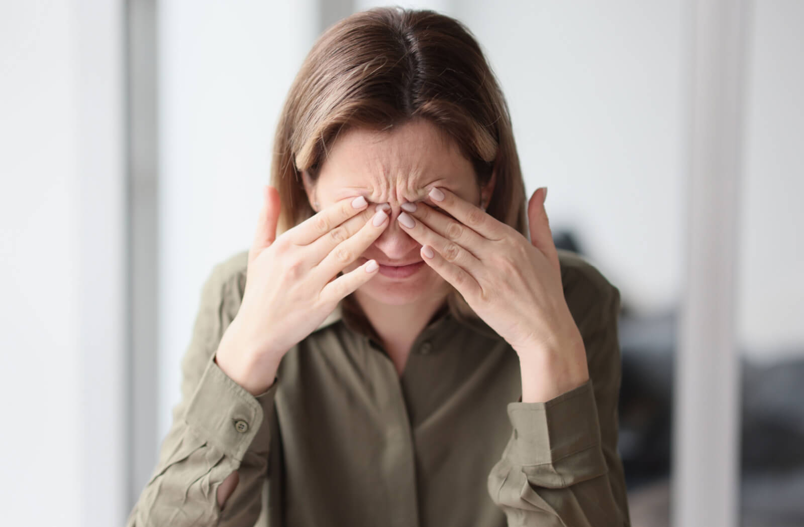 A woman in a olive-coloured top rubbing her eyes with both hands.