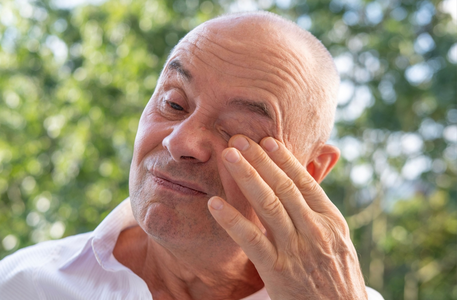 A mature individual rubs their eye due to dryness.