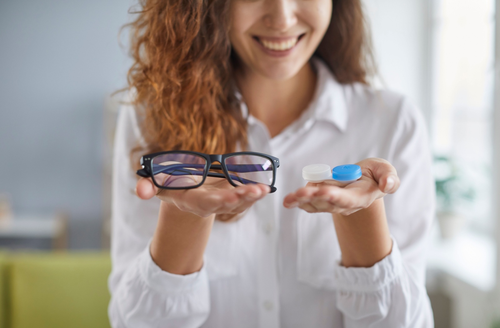 An optometrist holding a pair of glasses in one hand and a contact lens case in the other.