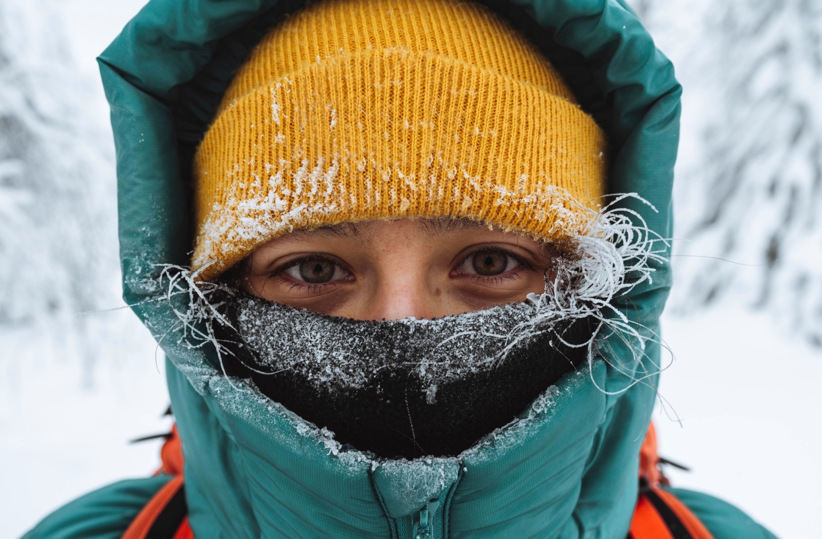 Close-up of a hiker bundled up in warm snow gear, a yellow toque and a black scarf covering their whole face save their eyes