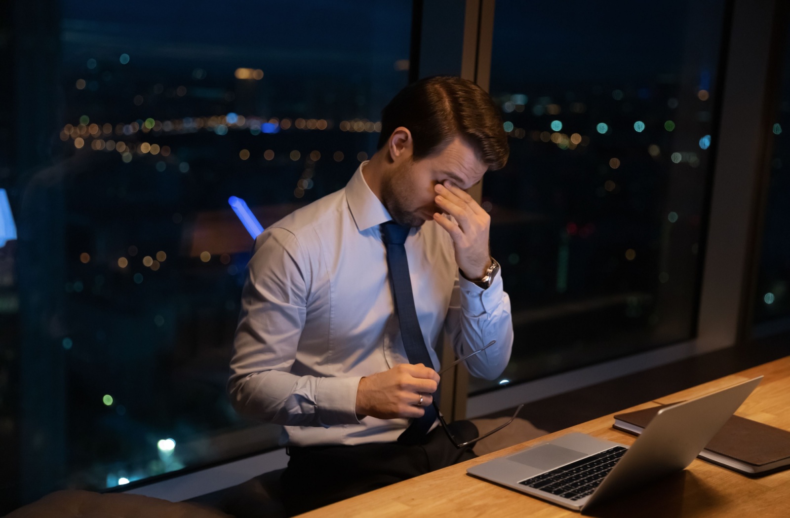 Man rubbing his eyes due to dry eyes discomfort while working late at a desk.