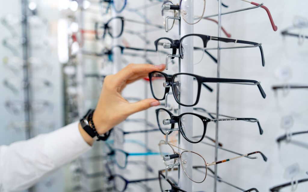 Person picking up a pair of eyeglasses at an opticians office, with a row of assorted glasses