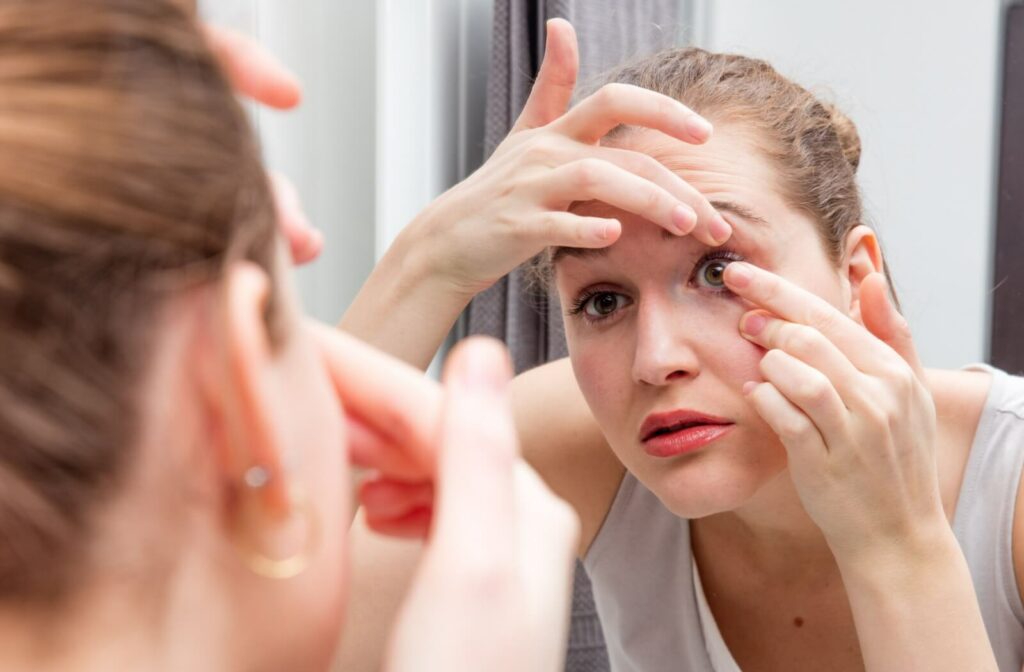 A young patient carefully removes their contact lens in front of the mirror to prepare for bed.