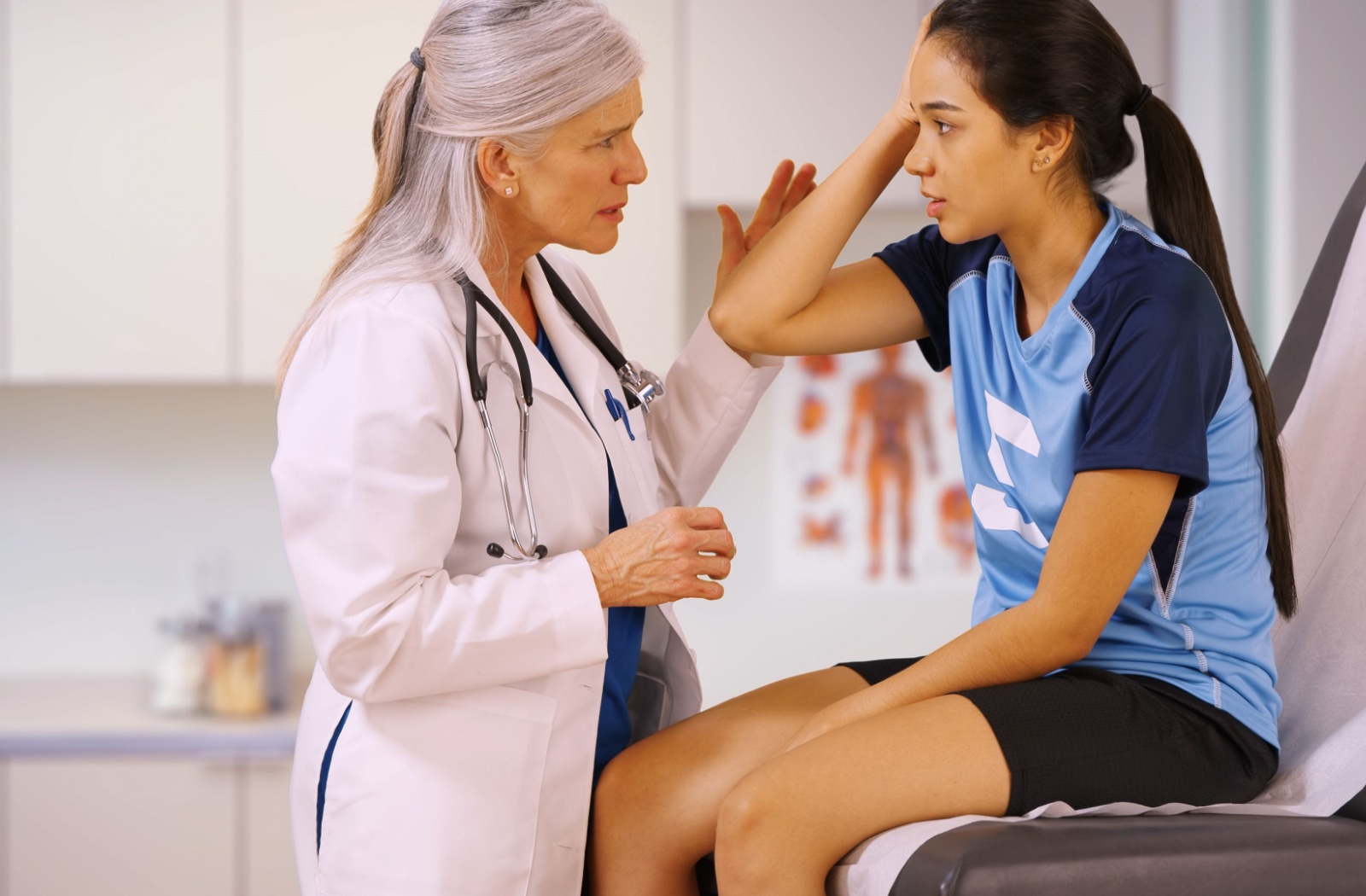 A doctor examines a young athlete holding their head during a medical appointment.