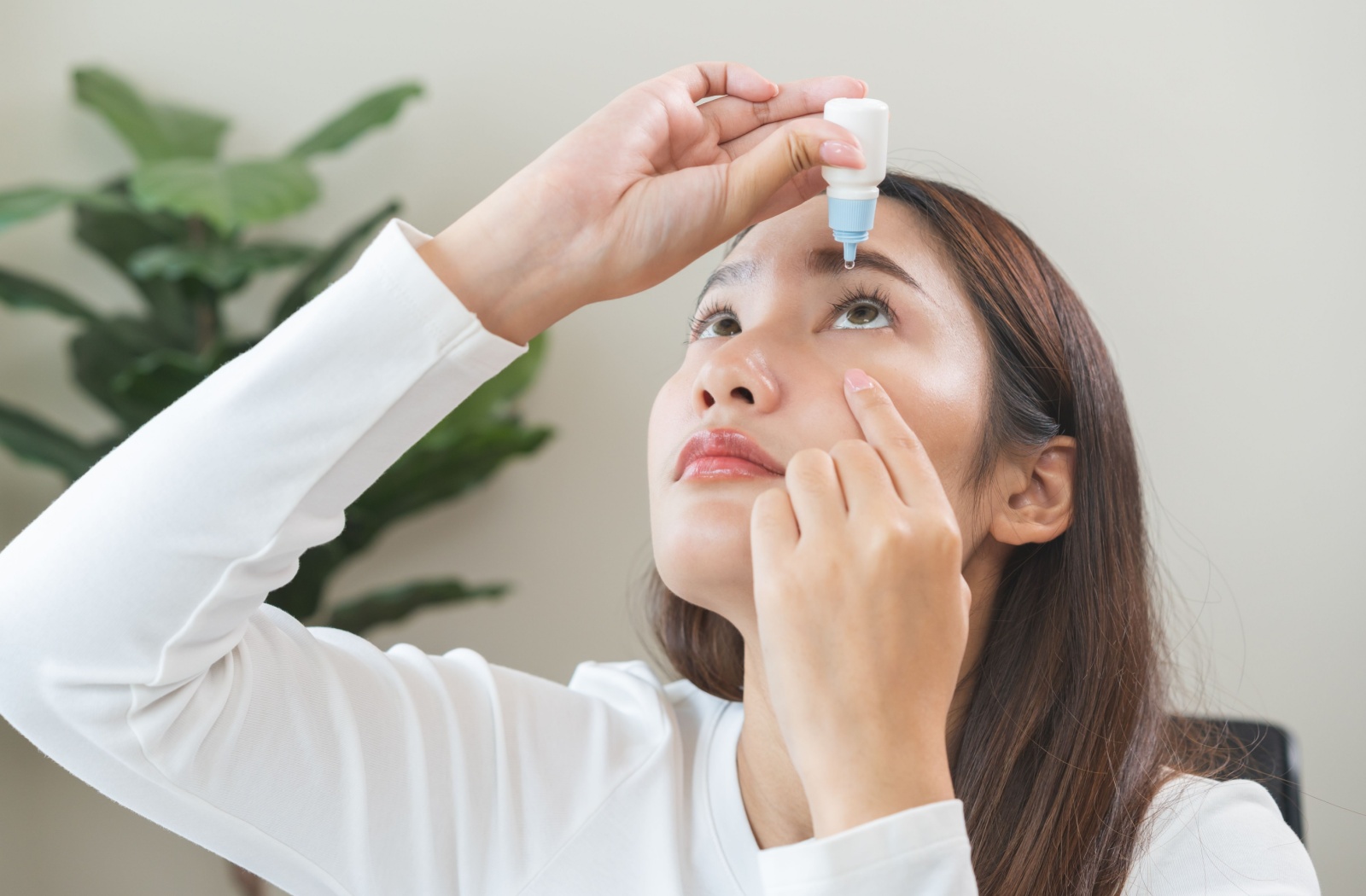 Young woman tilting her head back and applying moisturizing eye drops to relieve dryness or irritation.