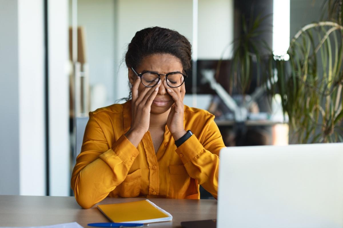 Person at a desk rubbing their eyes, suggesting eye strain or fatigue.